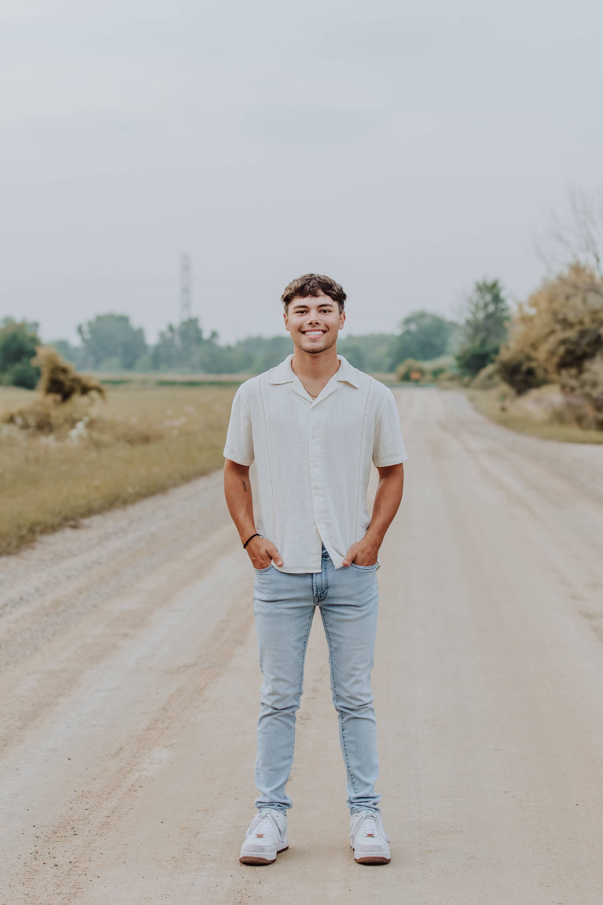 man in white shirt and light blue jeans standing on a dirt road